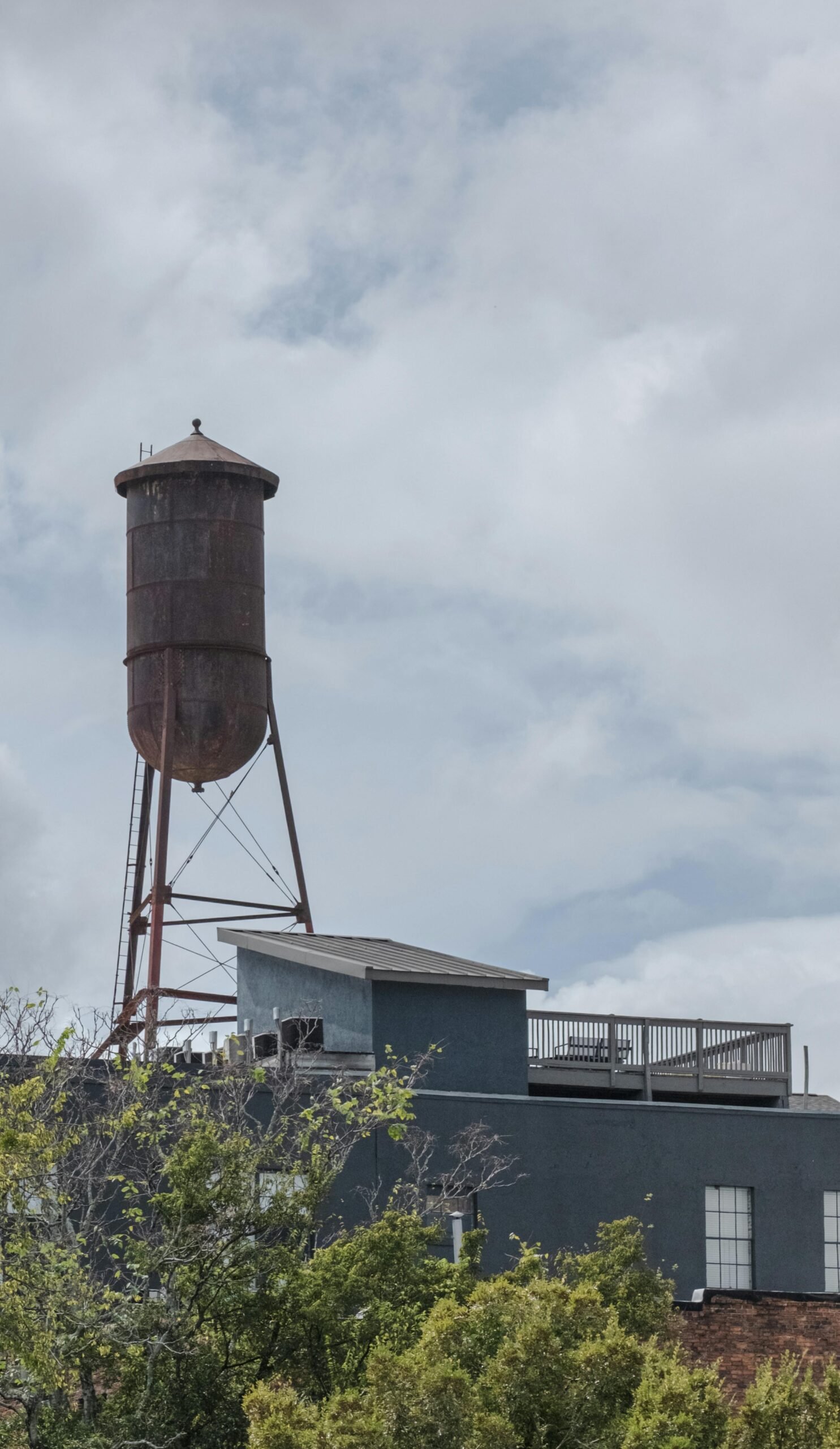 Rusty water tower atop an urban building in Macon, Georgia under a cloudy sky.